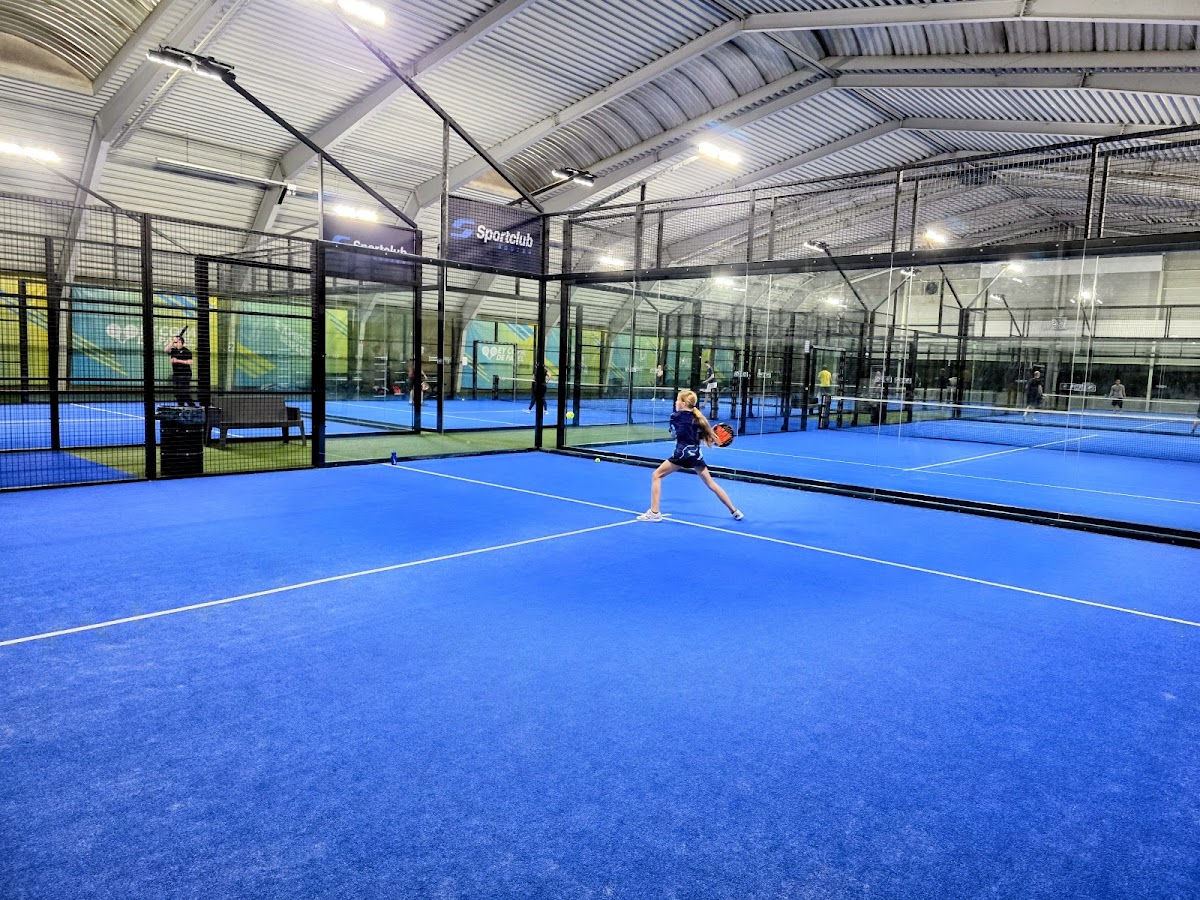 Binnenpadelclub met blauwe kunststof banen, speler in actie, moderne hal met LED-verlichting