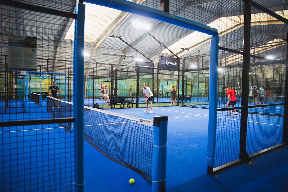 Overdekte padelclub met blauwe QuickPadel-banen, spelers in actie, professionele verlichting