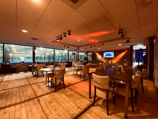 Moderne indoor padelbaan met gezellige bar en zitruimte, warm verlicht