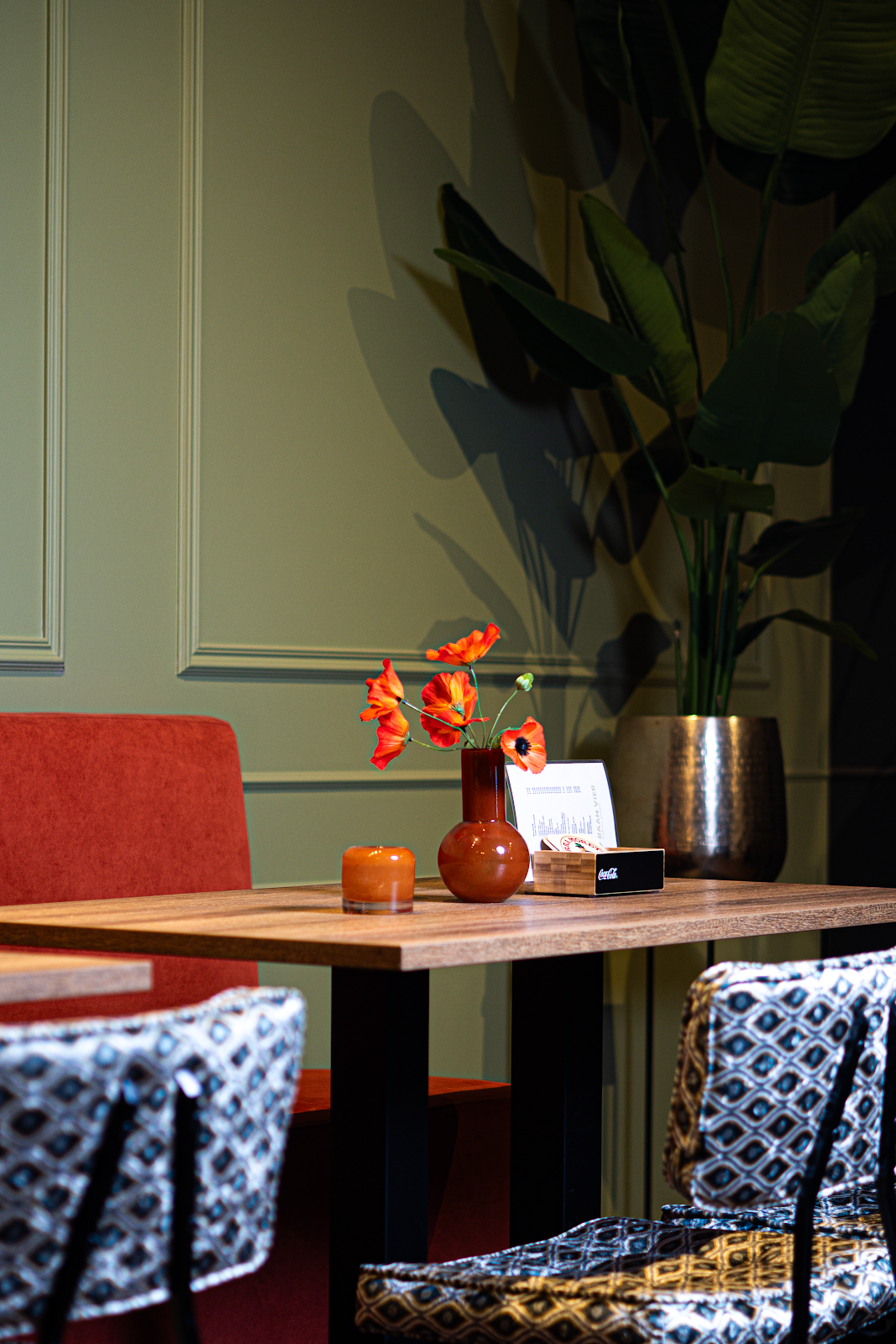 Elegante lounge met houten tafel, rode bloemen en design stoelen in padel clubhuis