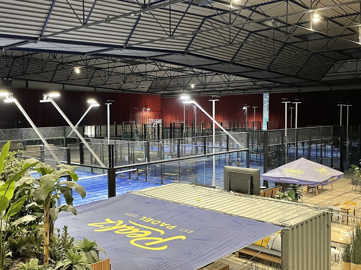 Moderne indoor padelclub met blauwe QuickPadel-banen, verlicht en voorzien van zithoek