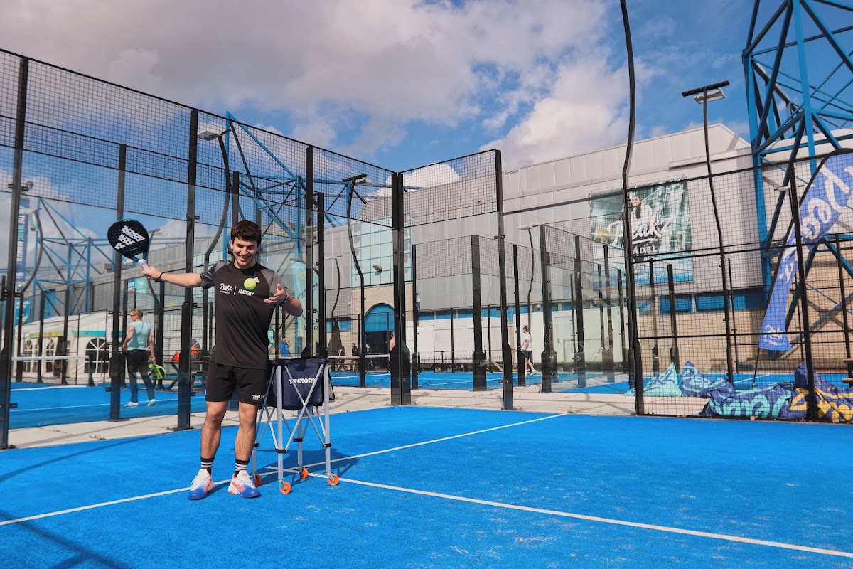 Padelbaan met blauwe ondergrond, speler met racket en stoel, zwarte hekken en moderne faciliteiten