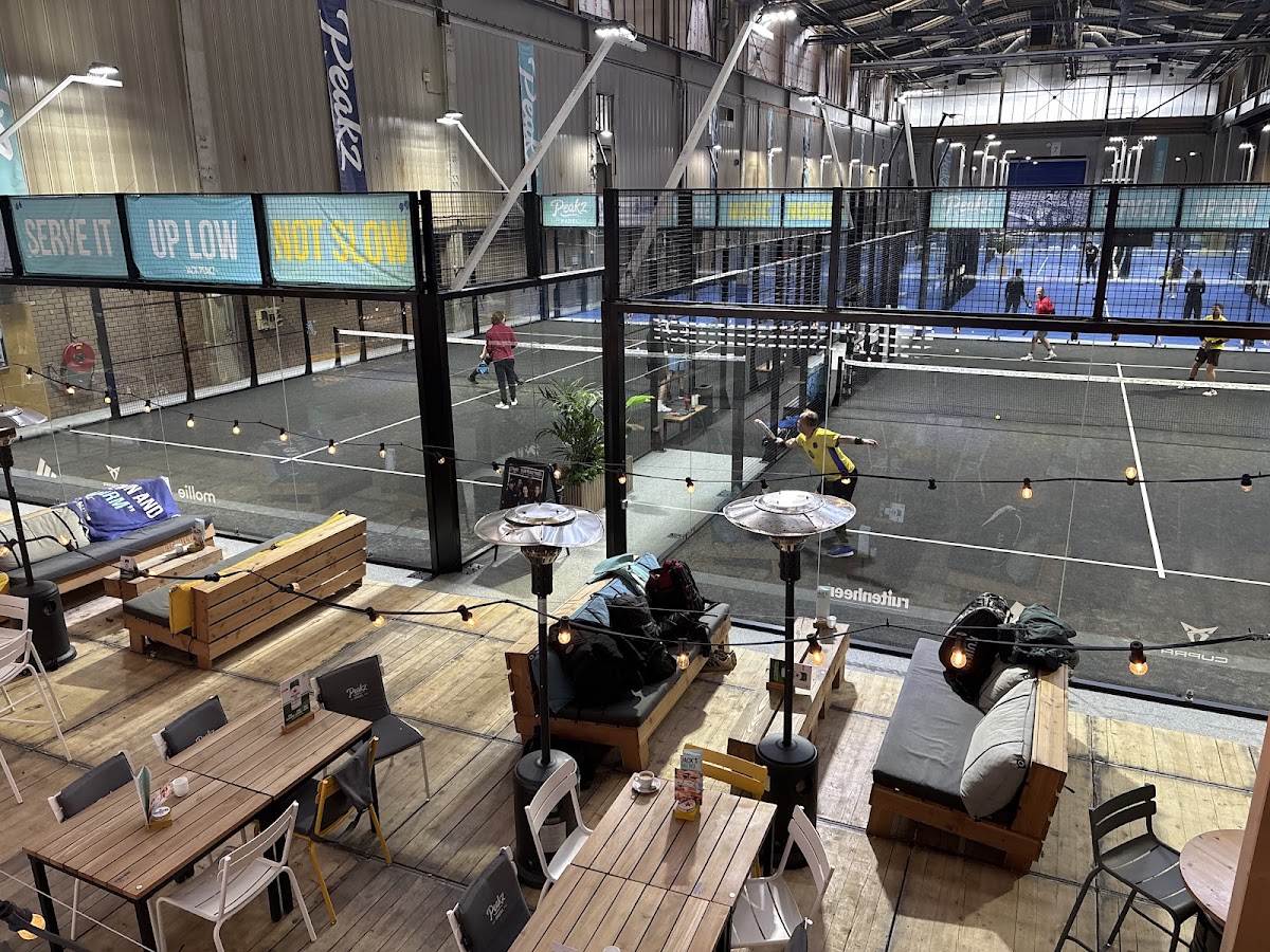 Overdekt padelcentrum met meerdere courts, houten zitgedeelte en speelende spelers