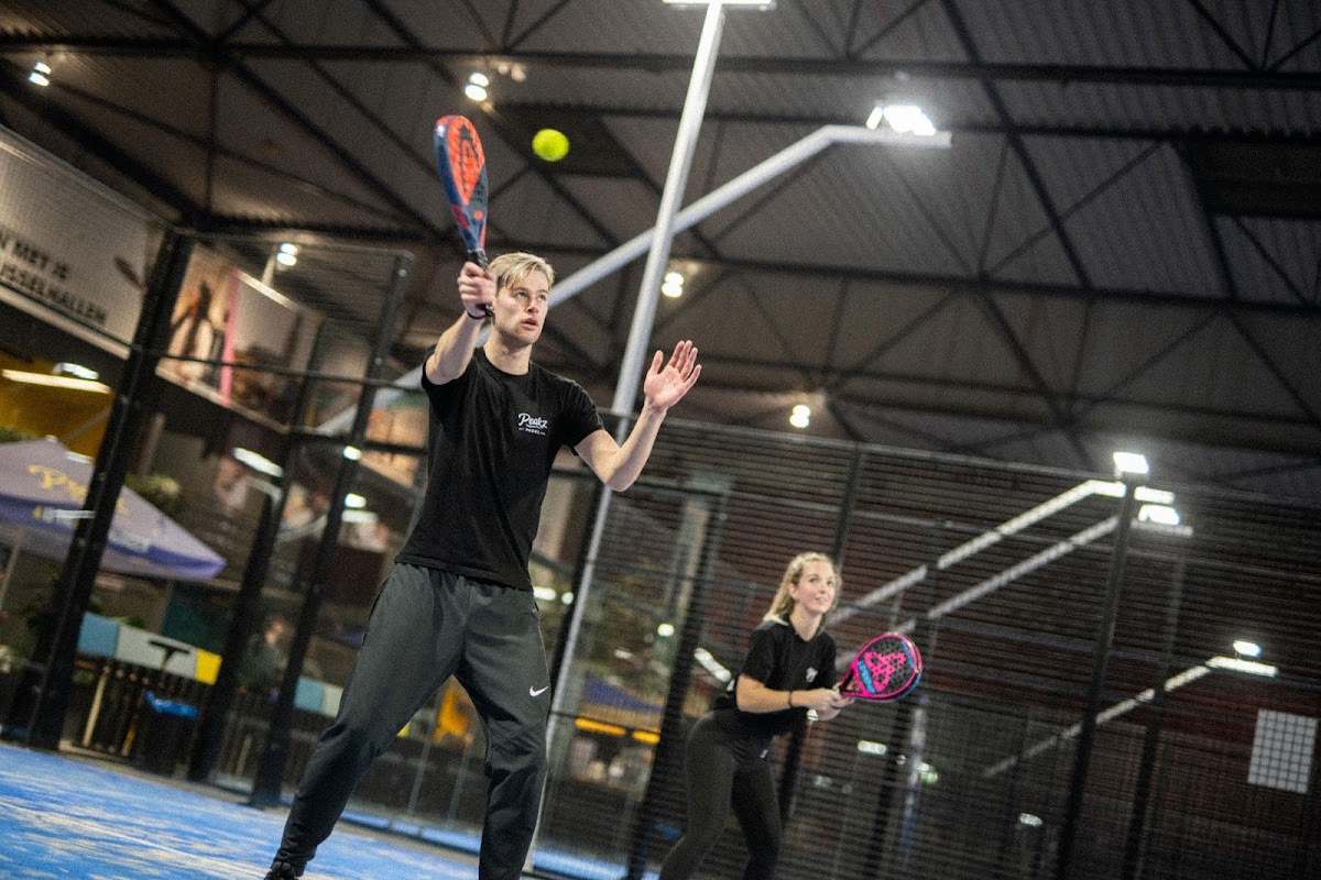 Padel spelers in actie op een binnenpadelbaan met blauwe hard court onder LED verlichting