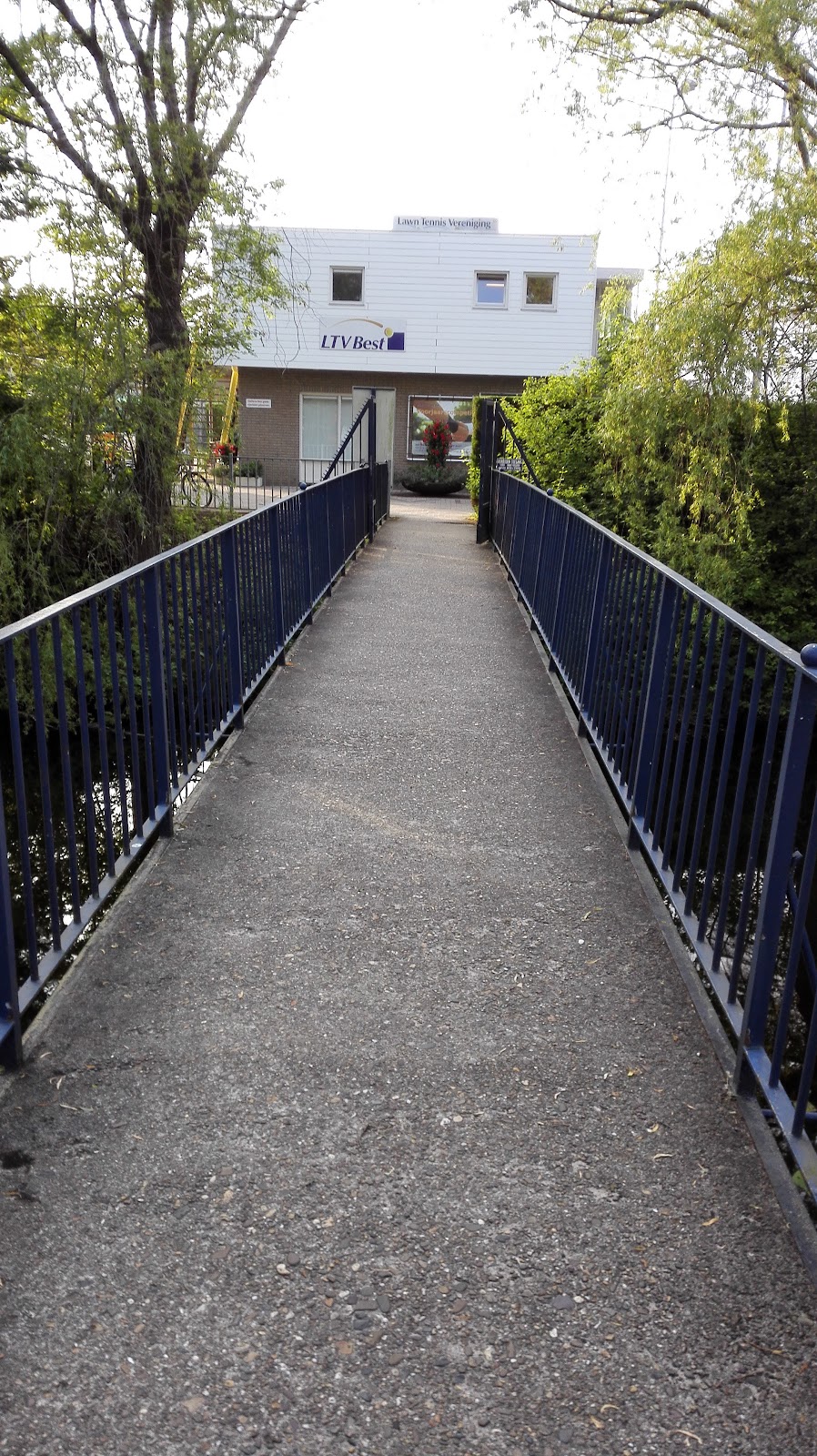 Ingang naar LIVBest padelbaan met blauw hek en gebouw op achtergrond