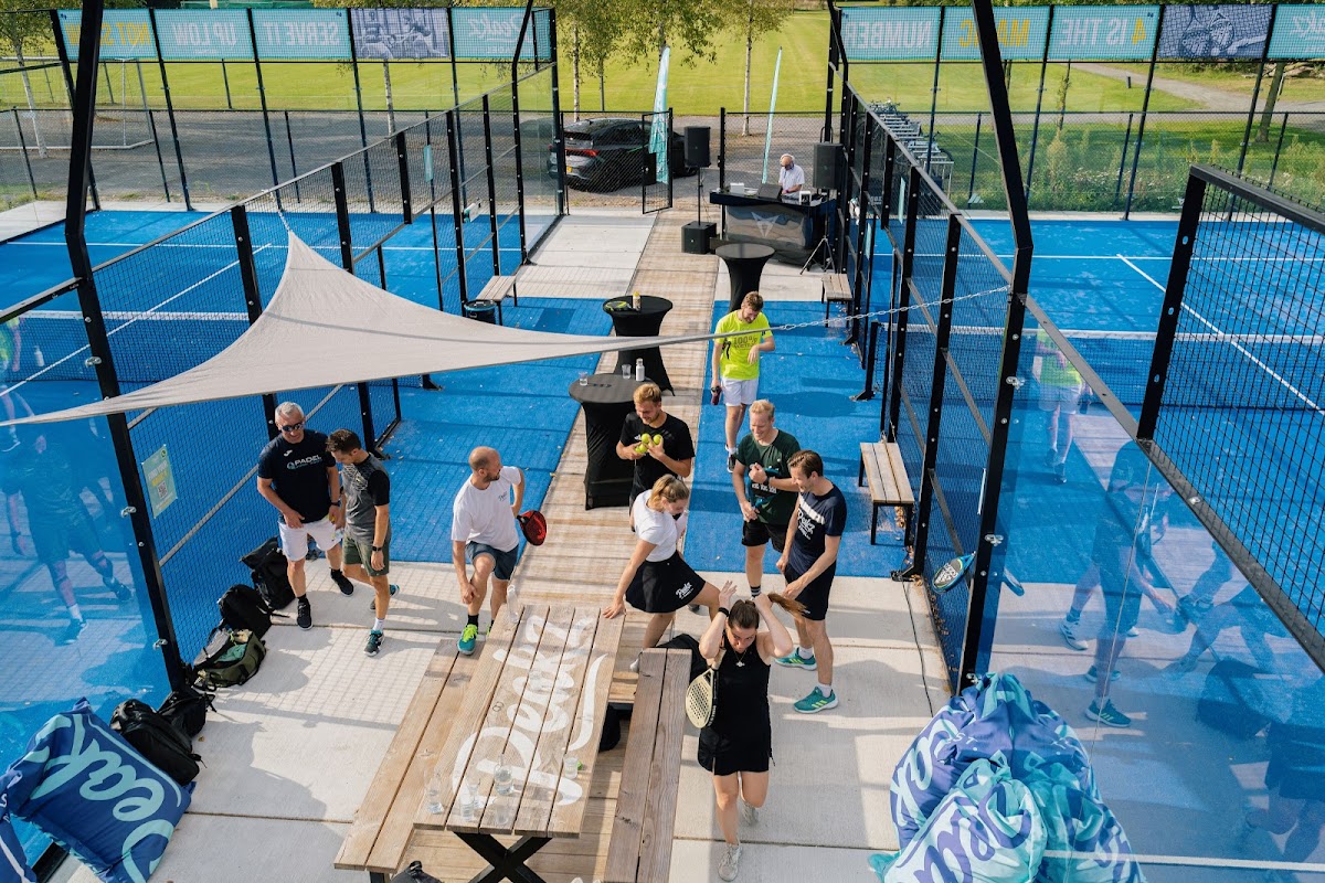 Outdoor padeltennisbanen met blauwe ondergrond, omgeven door zwart gaas en glas, met spelers in actie.