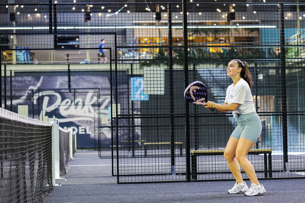 Vrouw speelt padel op indoor court met zwarte wanden en overhead verlichting