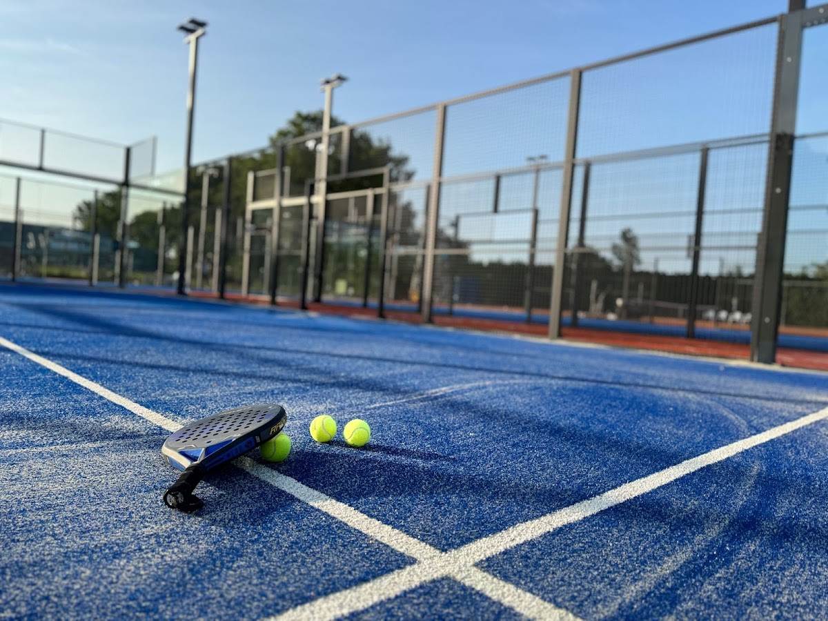 Padelracket met gele ballen op blauwe padelbaan met witte lijnen