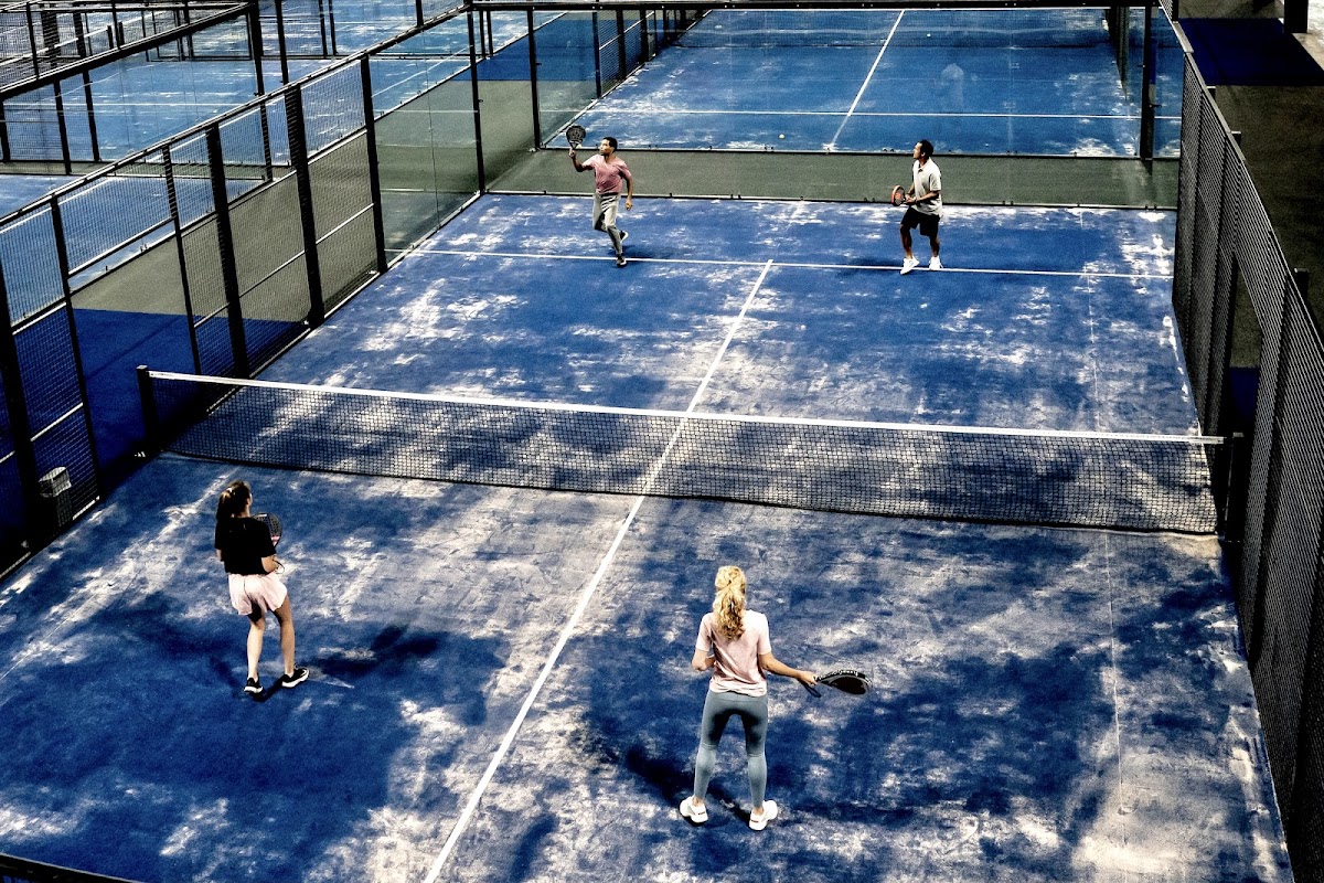 Padelbanen buiten met blauwe hardcourt ondergrond, spelers in actie op meerdere velden.