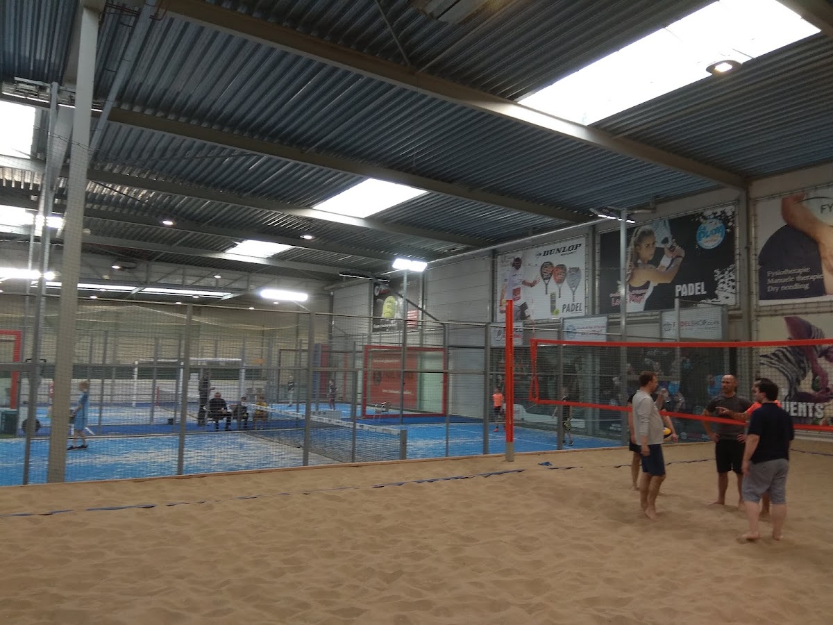 Indoorpadelclub met blauwe hardcourt, rode omheiningen en spelers in de faciliteit