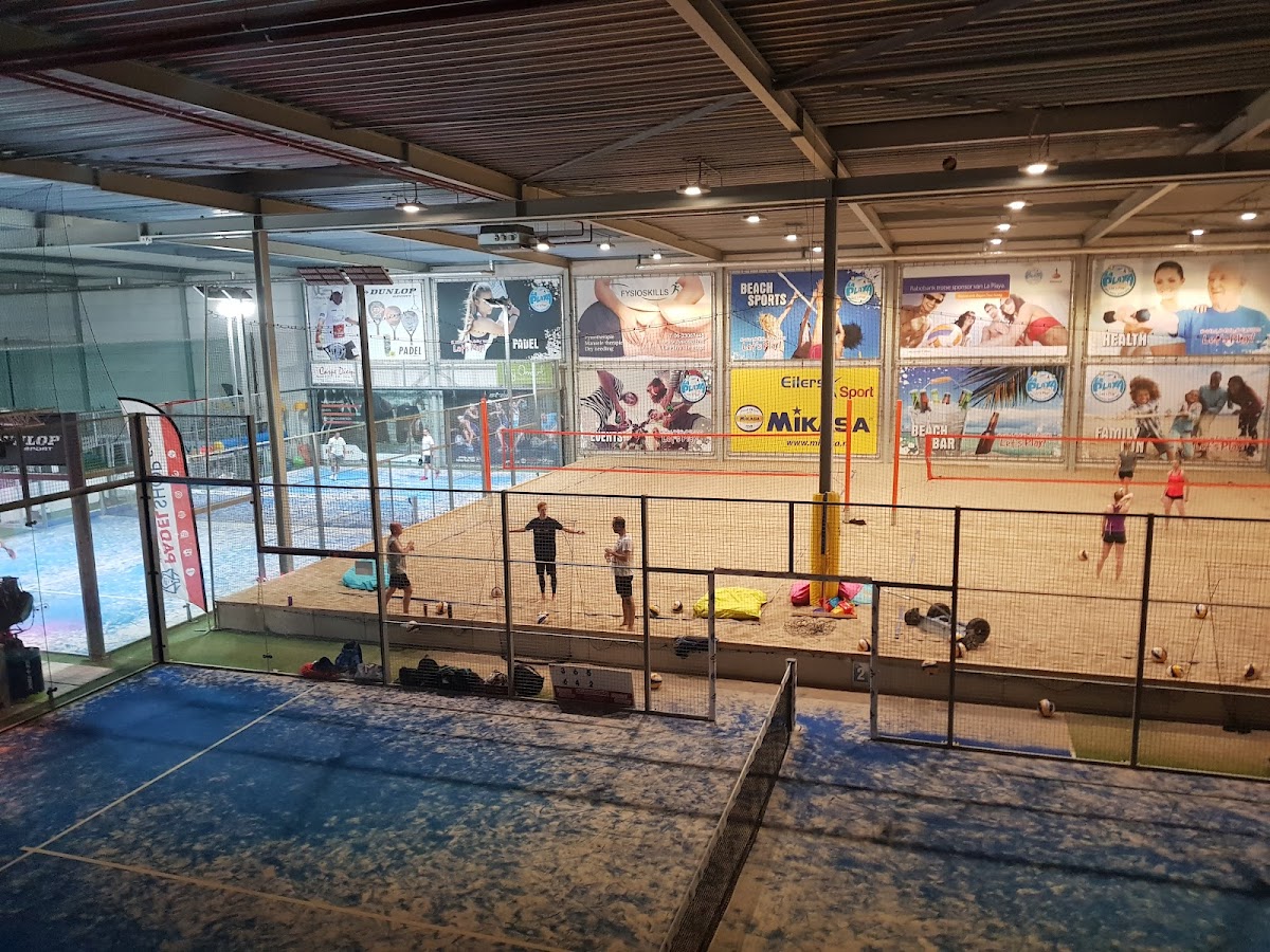 Binnenpadelclub met meerdere zandvelden, netting en verlichting, speelende kinderen zichtbaar