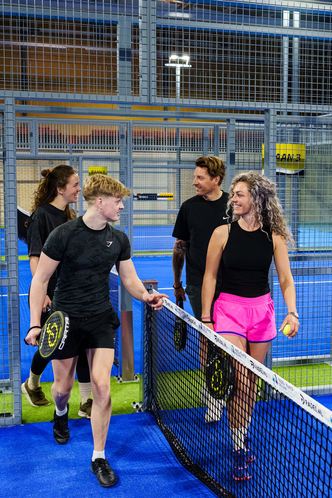 Groep spelers bij padelnetten op kunstgrasbaan met blauwe ondergrond in overdekte hal