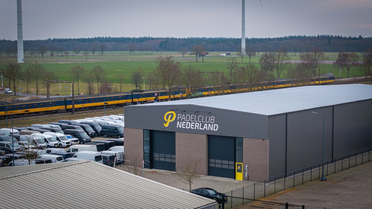 Padelclub Nederland faciliteit met parkeerplaats, treinspoor en groene velden op achtergrond