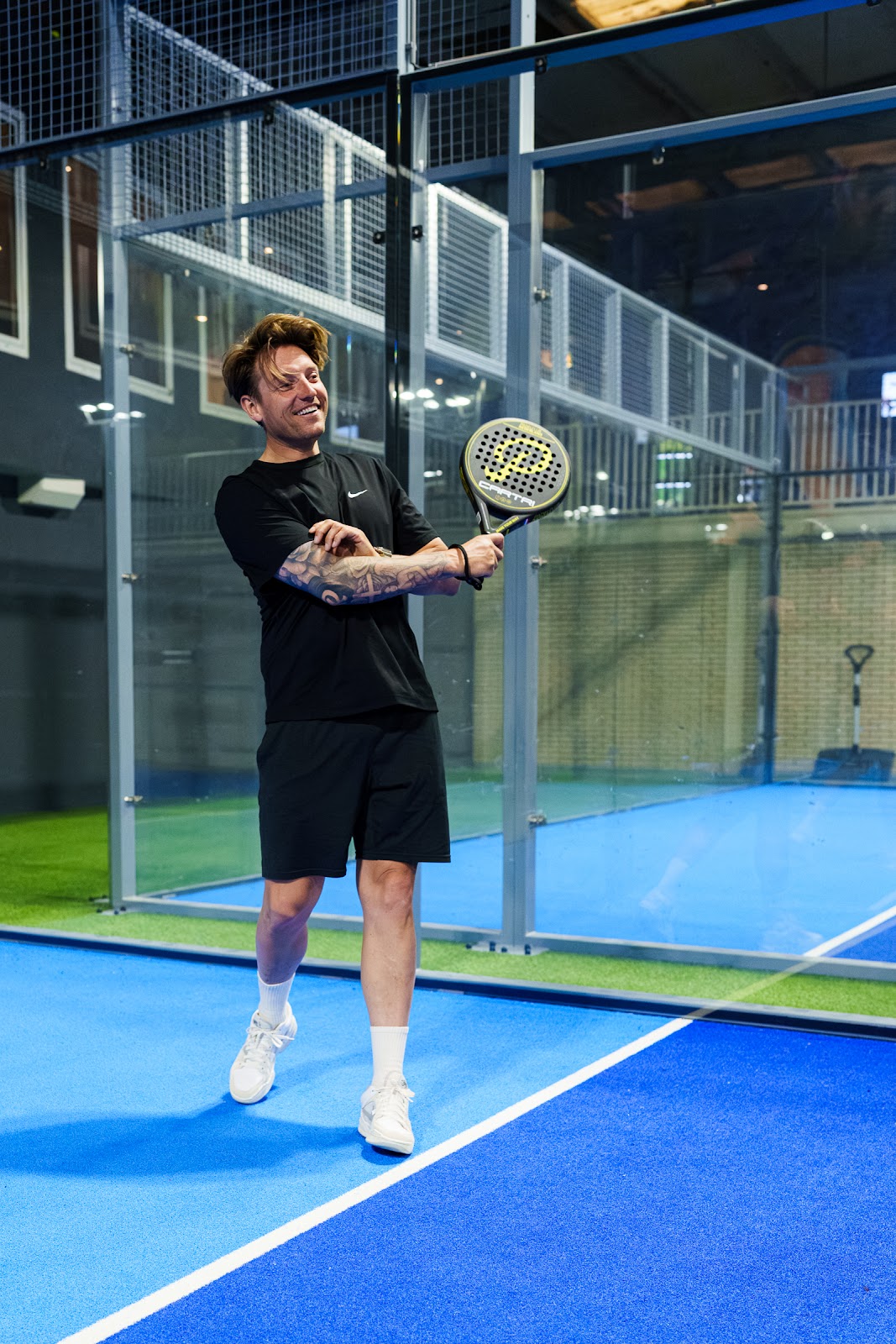 Padelspeler in actie op blauwe binnenbaanveld met glazen wanden