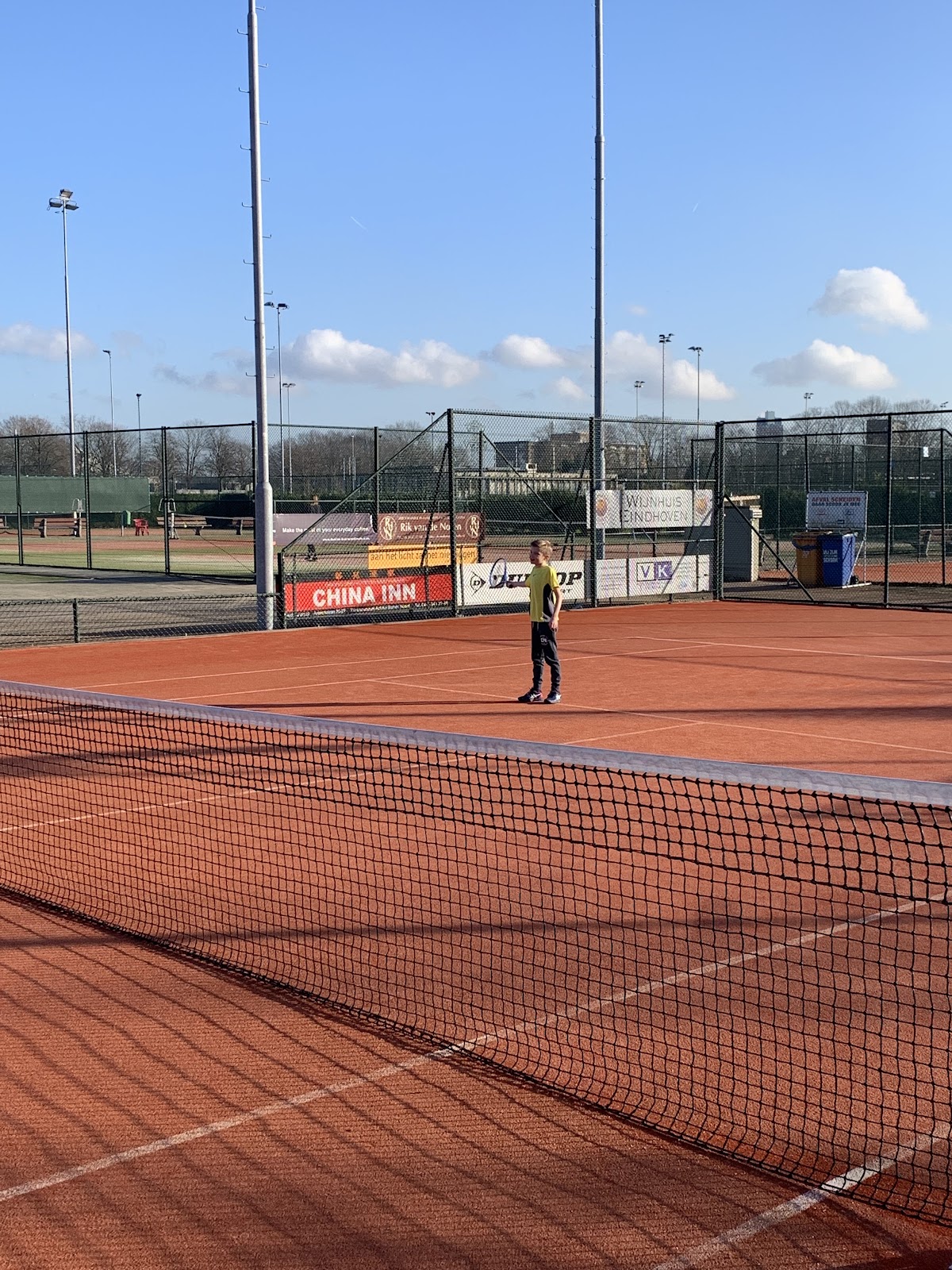 Buitenpadelbaan met rood tapijt, net op voorgrond, sponsorborden en floodlights zichtbaar
