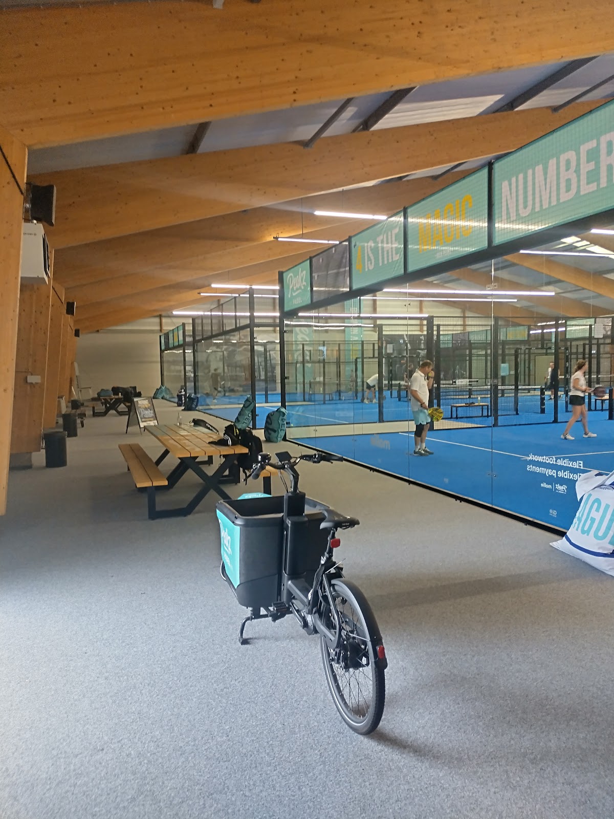 Binnenpadelclub met blauwe velden, fietsen en houten plafond met verlichting