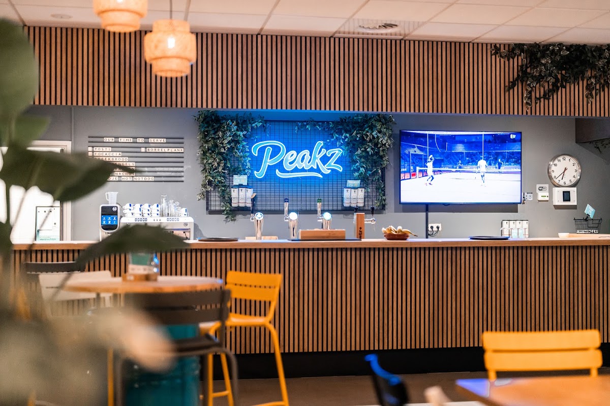 Moderne padelbaan clubhuis met Peakz neonbord, bar en gele stoelen