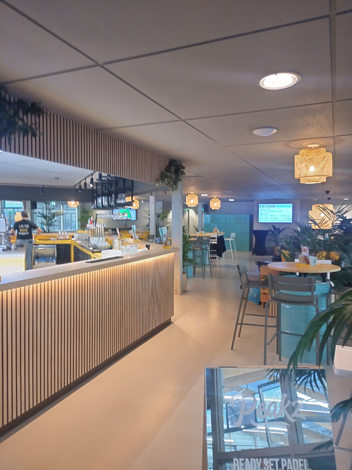 Moderne indoor padelbaan met bar, gele accenten en plantendecoratie
