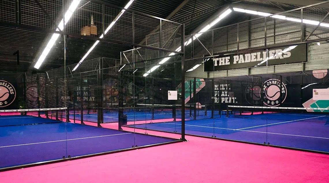 Moderne indoor padelclub 'The Padellers' met blauwe en roze kunststof courts en lineaire verlichting