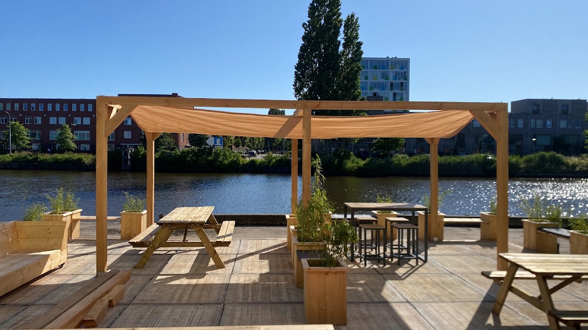 Waterfront padel club met houten pergola's, zitplaatsen en bar aan rivier