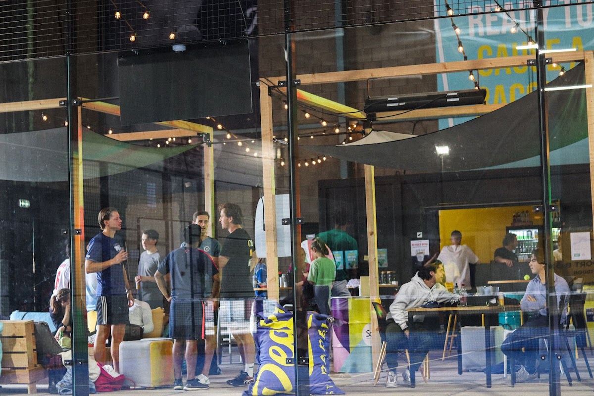 Padel club met glazen wanden, houten constructie, verlichting en bezoekers in en buiten de baan