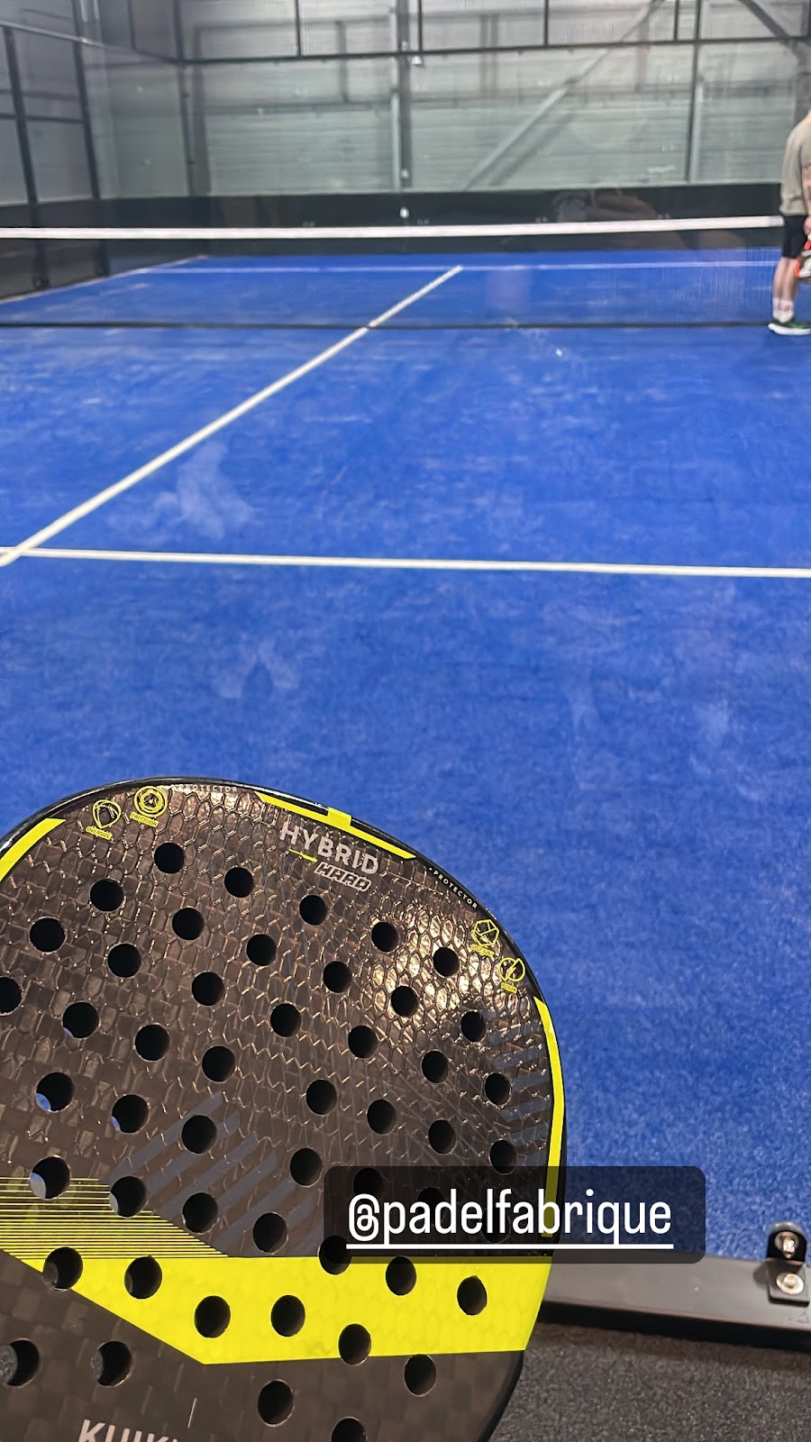 Padelbaan met blauwe hardcourt en hybride racket op indoor padel club