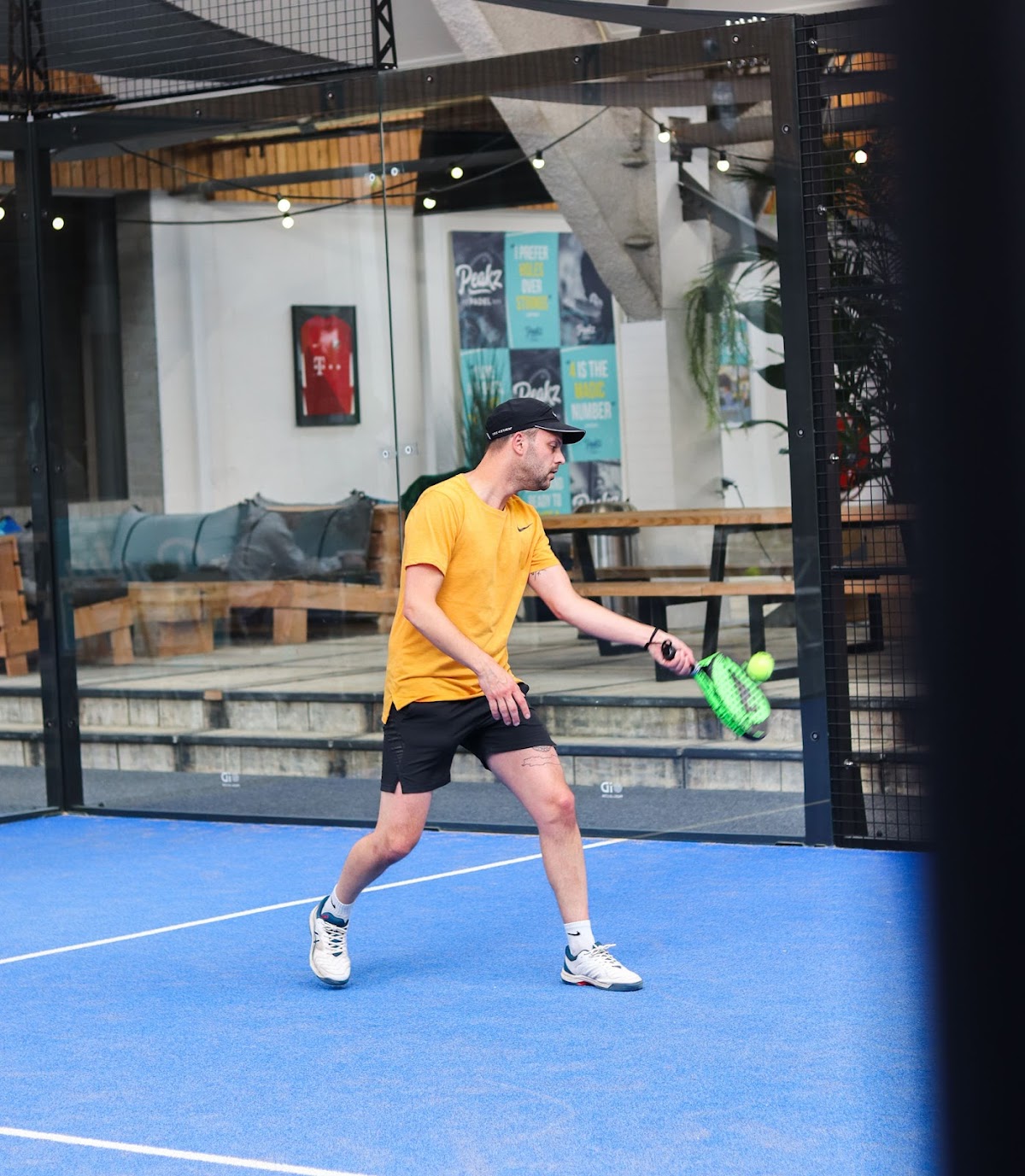 Padelspeler in geel shirt op blauwe baan in moderne indoor padelbaan