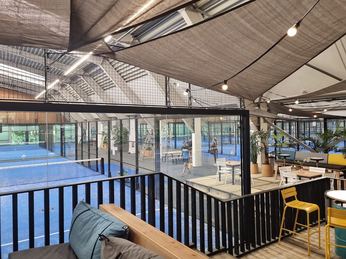 Overdekte padelbanen met blauwe hardcourt en lounge-area met zithoeken