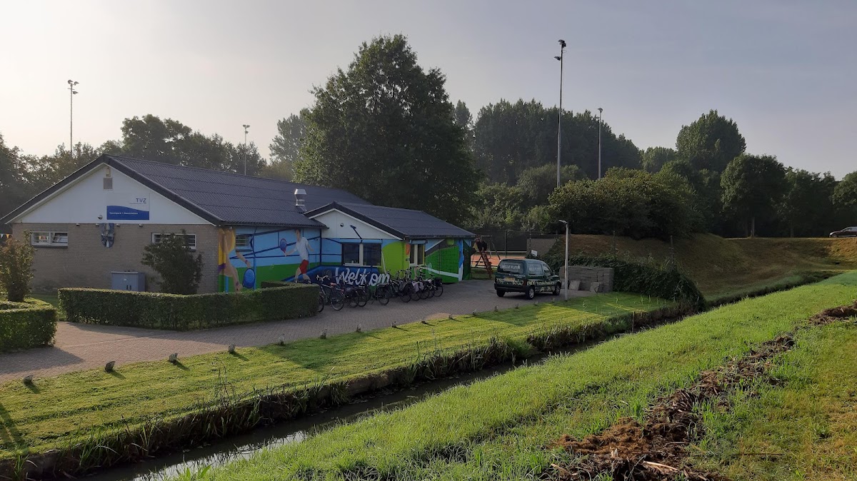 Padel- of sportcomplex met gebouwen, grasland en sloot, zonder zichtbare speelvelden