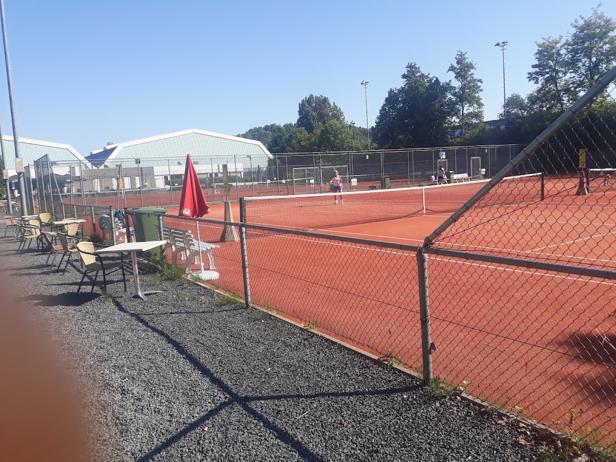 Outdoor padelclub met meerdere rode courts, zithoeken en verlichtingsmasten onder blauwe hemel