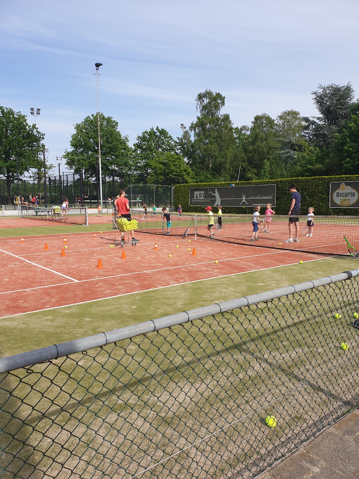 Outdoor padelclub met groene kunstgras courts, trainers en kinderen spelen, verlichting zichtbaar