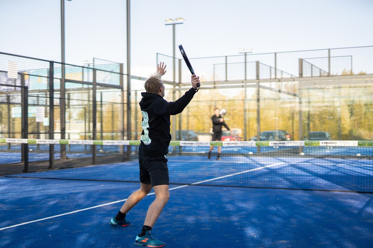 Padelspeler in actie op blauwe buitenbaan met floodlights en omheining