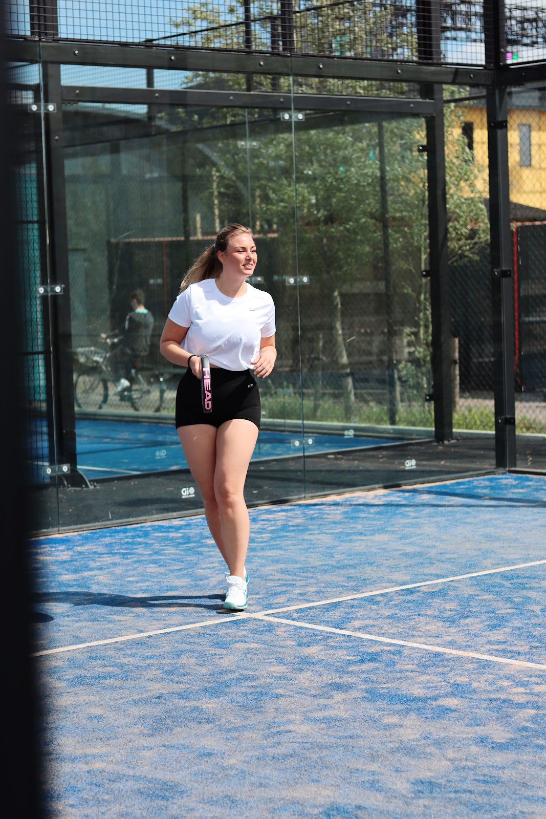 Vrouw joggend op blauwe padelbaan met glazen wanden en groene omgeving