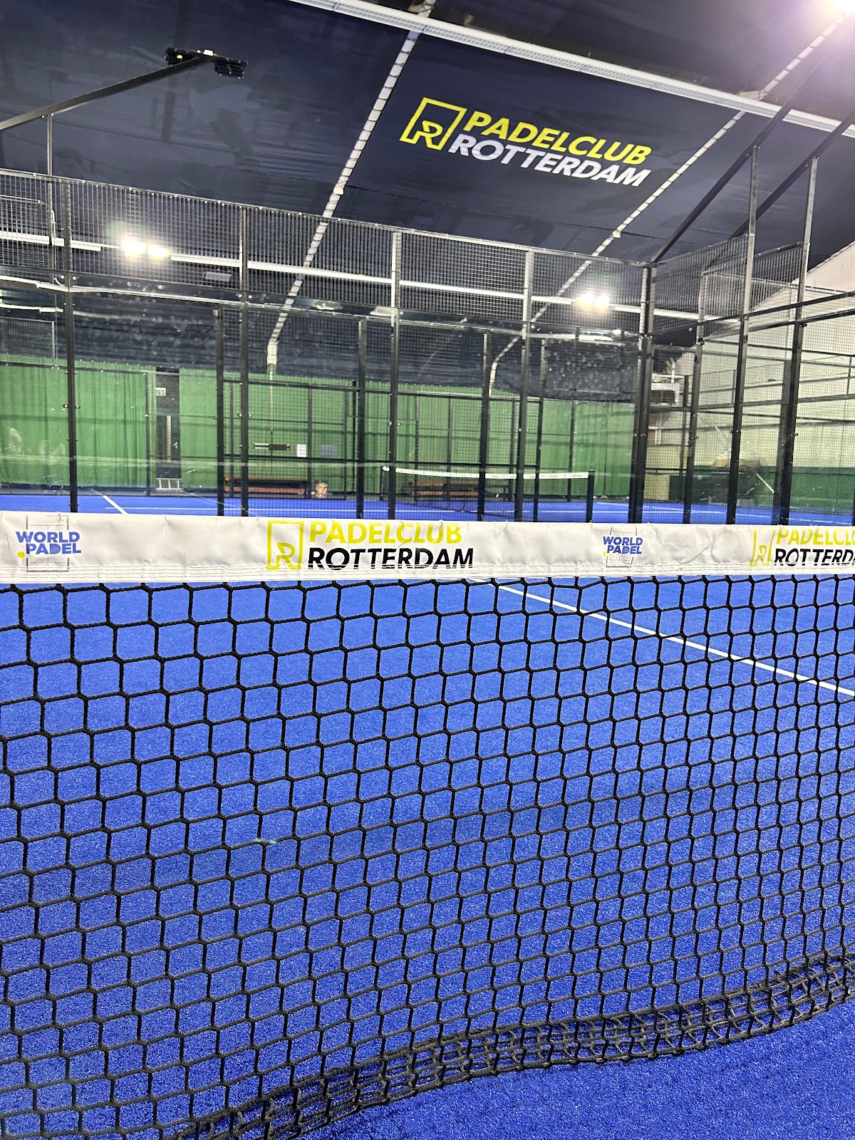 Padelclub Rotterdam indoorbaan met blauw hardcourt en net, professionele verlichting