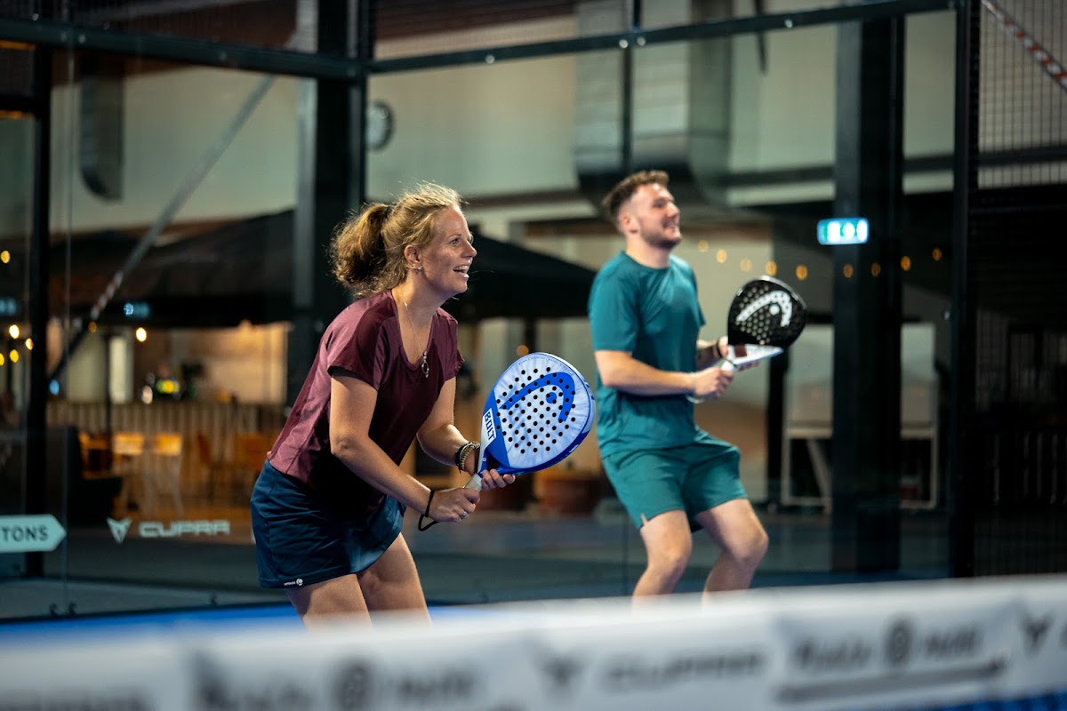 Twee padelers spelen op een indoorbaan met blauwe en zwarte rackets