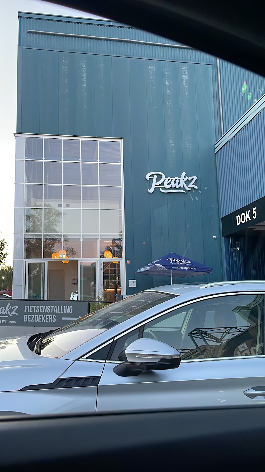 Peakz padel club met moderne blauwe hal, grote ramen en ingang met terras