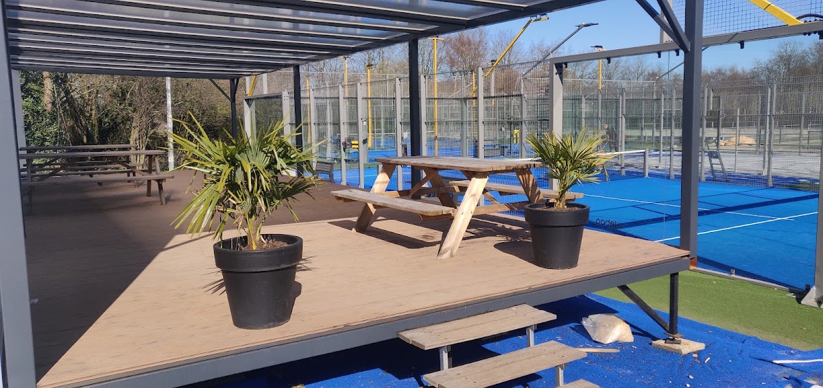 Outdoor padelclub met blauwe velden, zithoek onder afdak en groene planten