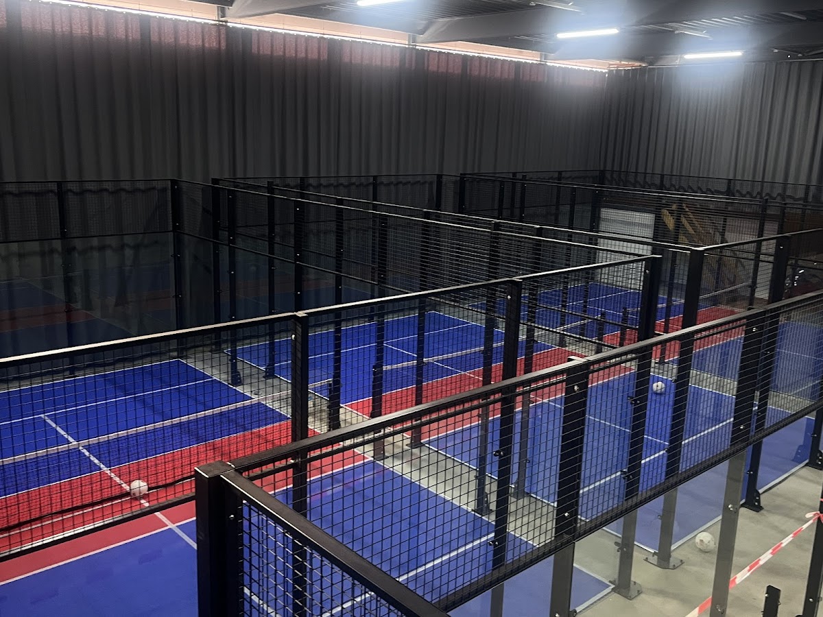 Indoor padelclub met meerdere courts, blauwe en rode ondergronden, zwarte netting