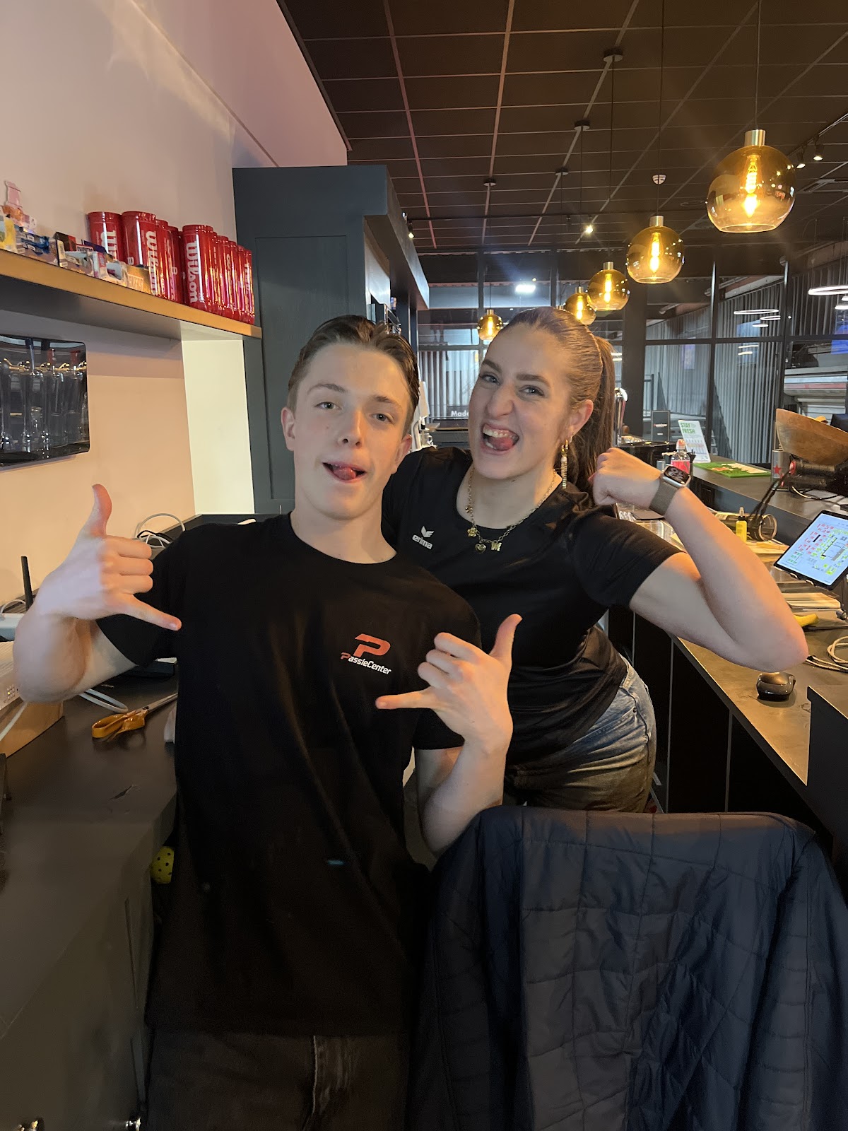 Twee jonge mensen poseren lachend in een padel club met gouden hangende lampen