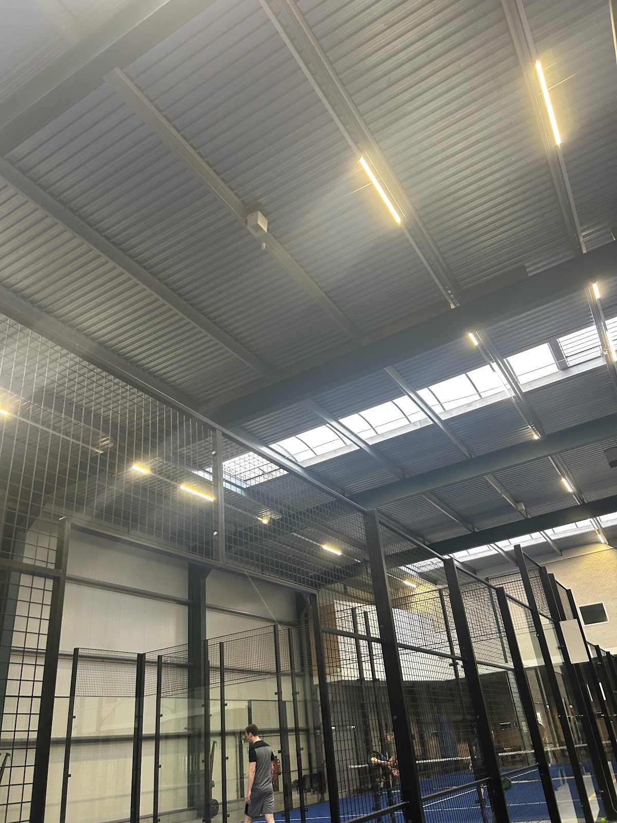 Binnenpadelclub met blauwe courts, zwarte omheiningen en LED-verlichting aan het plafond