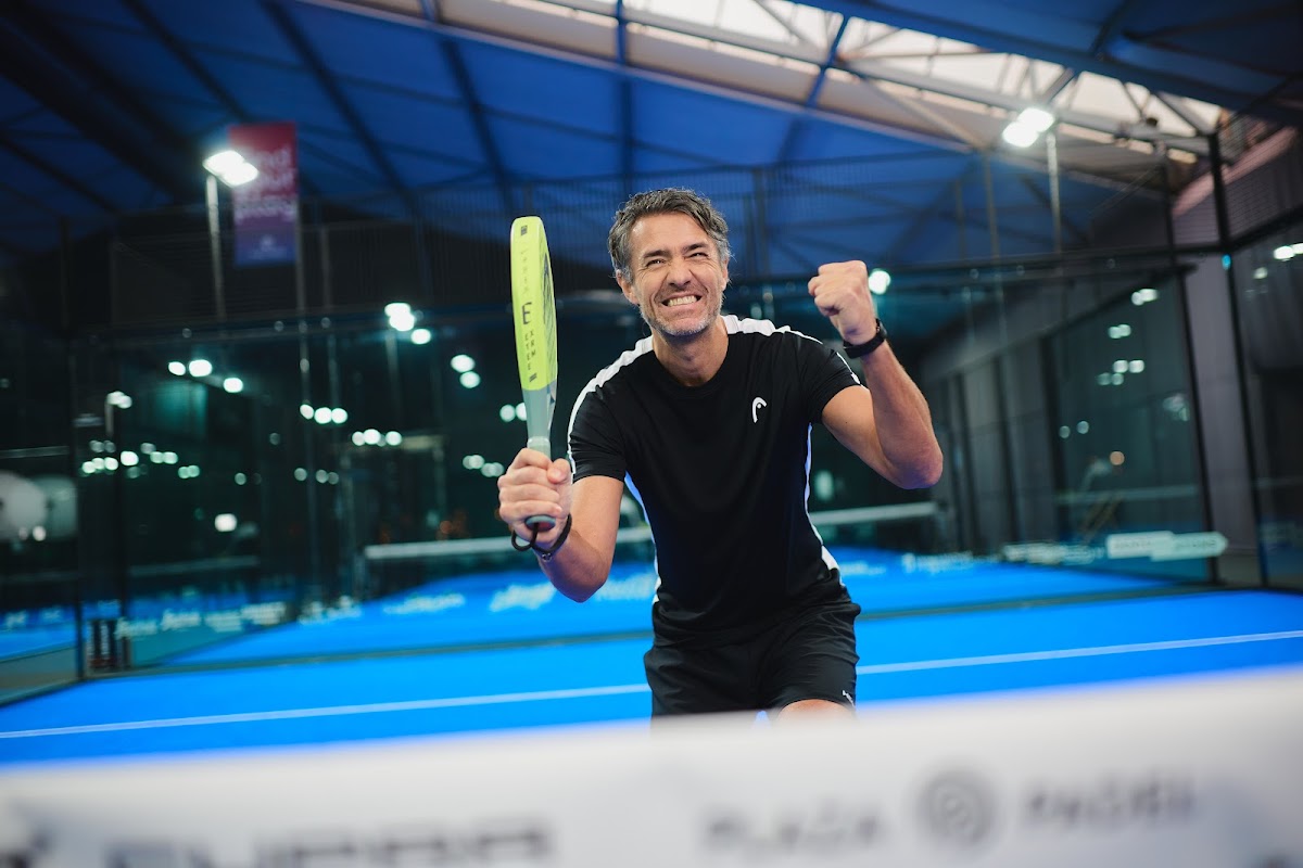 Padelspeler in actie op blauwe binnenbaan met LED-verlichting 's avonds