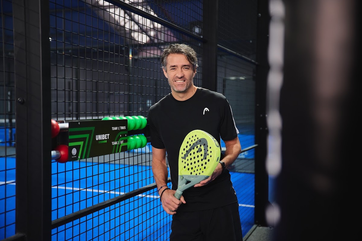 Padelspeler met geel racket op blauwe indoorbaan met zwarte netten