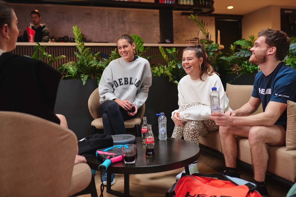 Groep vrienden ontspant in padel club lounge met planten en drankjes
