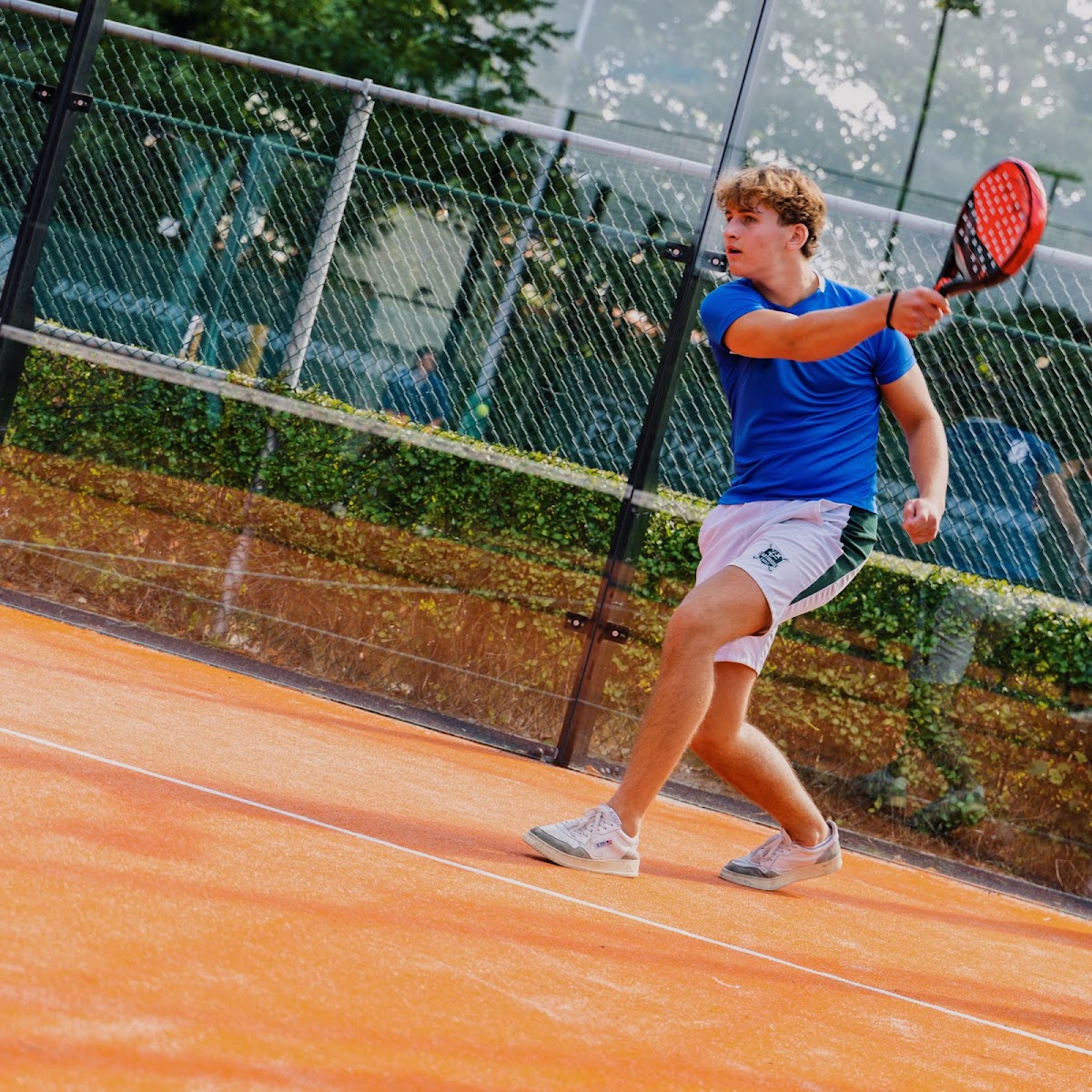 Jonge tennisser speelt op oranje padelbaan met netwerk op achtergrond