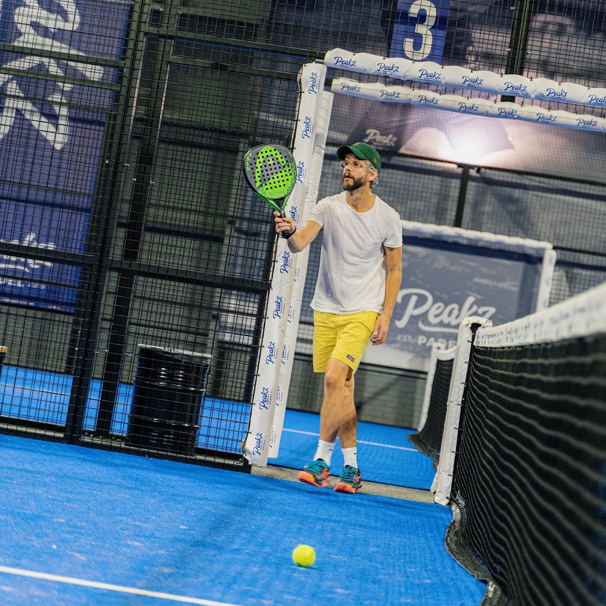 Padelspeler met groene racket op blauwe indoorbaan in Peakz-faciliteit