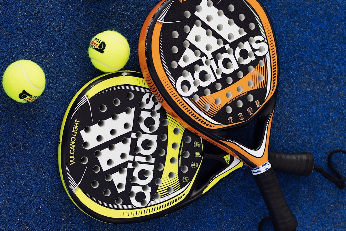 Adidas padelrackets en tennisballen op blauwe ondergrond