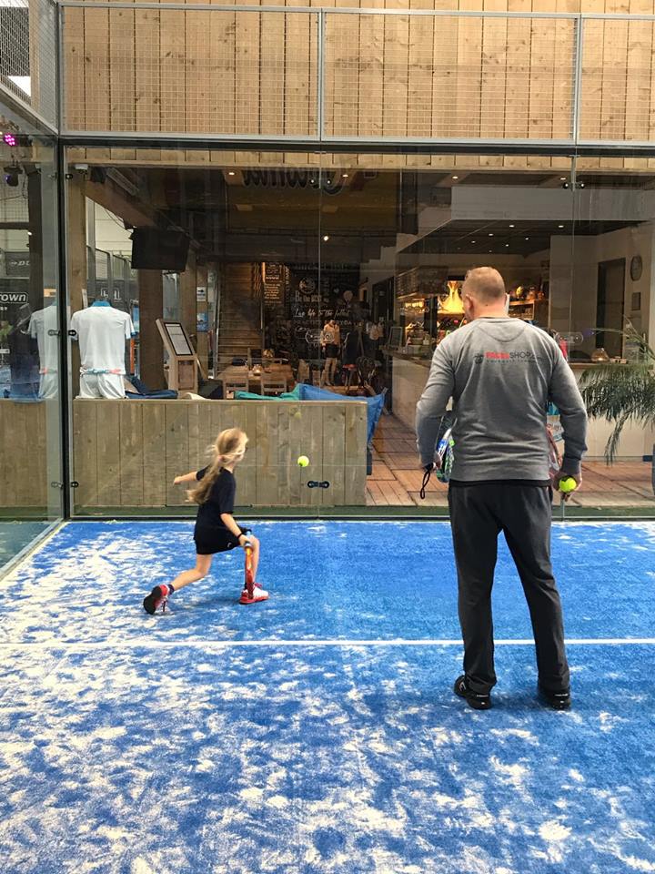 Padelspelers in actie op blauwe buitenbaan met terras op achtergrond