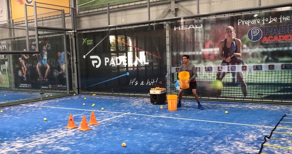 Padelbaan met blauwe QuickPadel-ondergrond, oranje ballenemmers en trainingsconussen