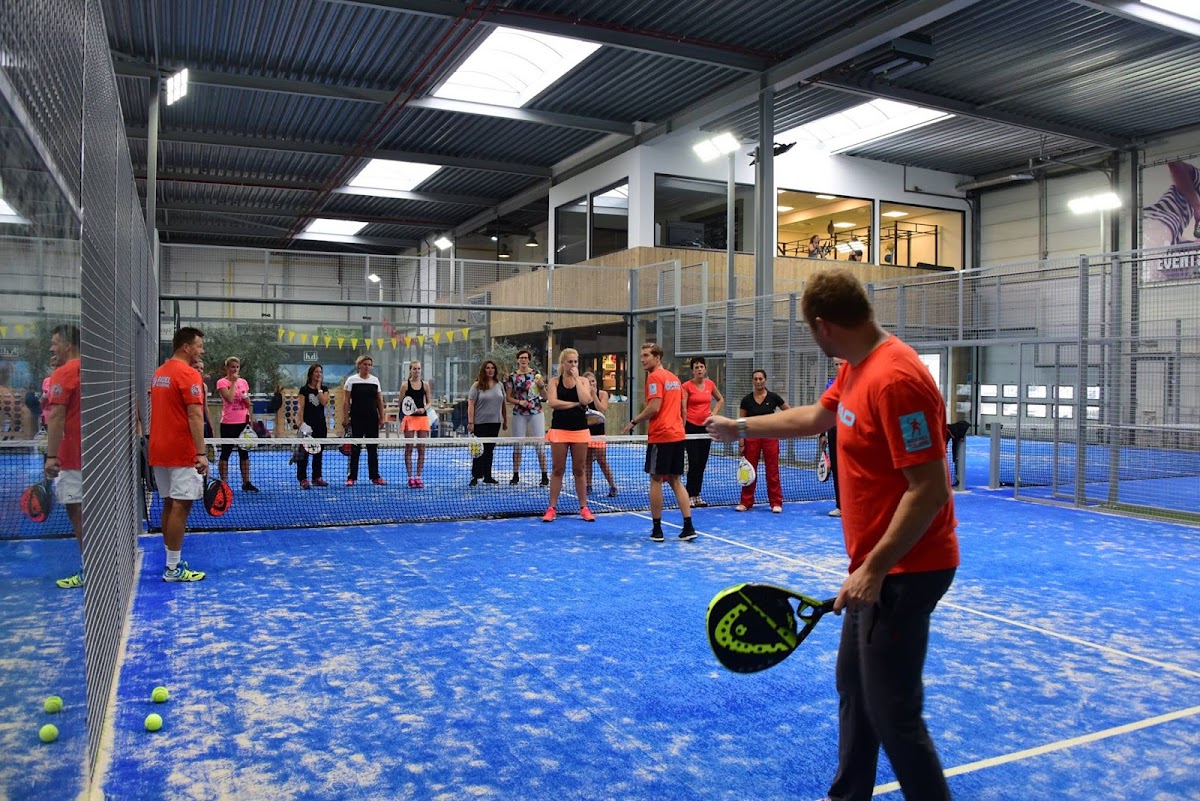 Padelclub met blauwe QuickPadel-baan, instructeur en groep spelers in rode shirts