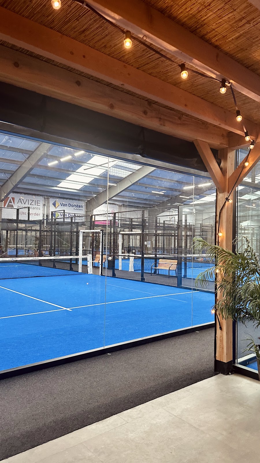 Indoor padelclub met blauwe QuickPadel-banen, houten balken en moderne verlichting
